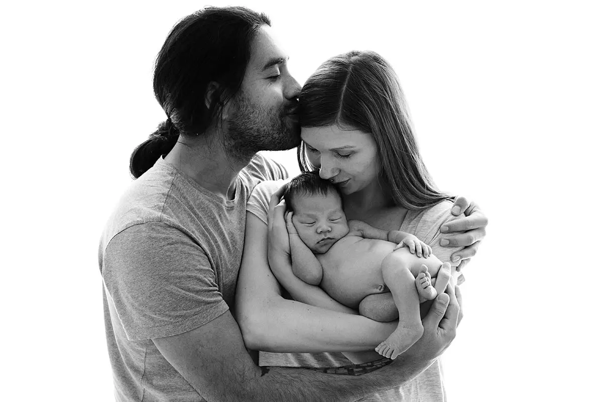 Black and white portrait of parents holding their newborn baby, showcasing an intimate and minimalist style.
