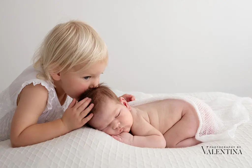 sister kissing newborn sister on the head while sleeping on her tummy during a shoot in London