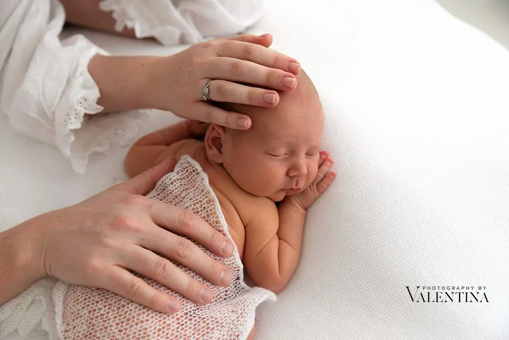 portrait of a newborn sleeping on his tummy. Mum and dad have their hands on his back and head.