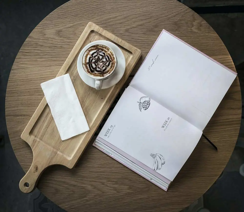 table with a pregnancy journal and a cup of coffee