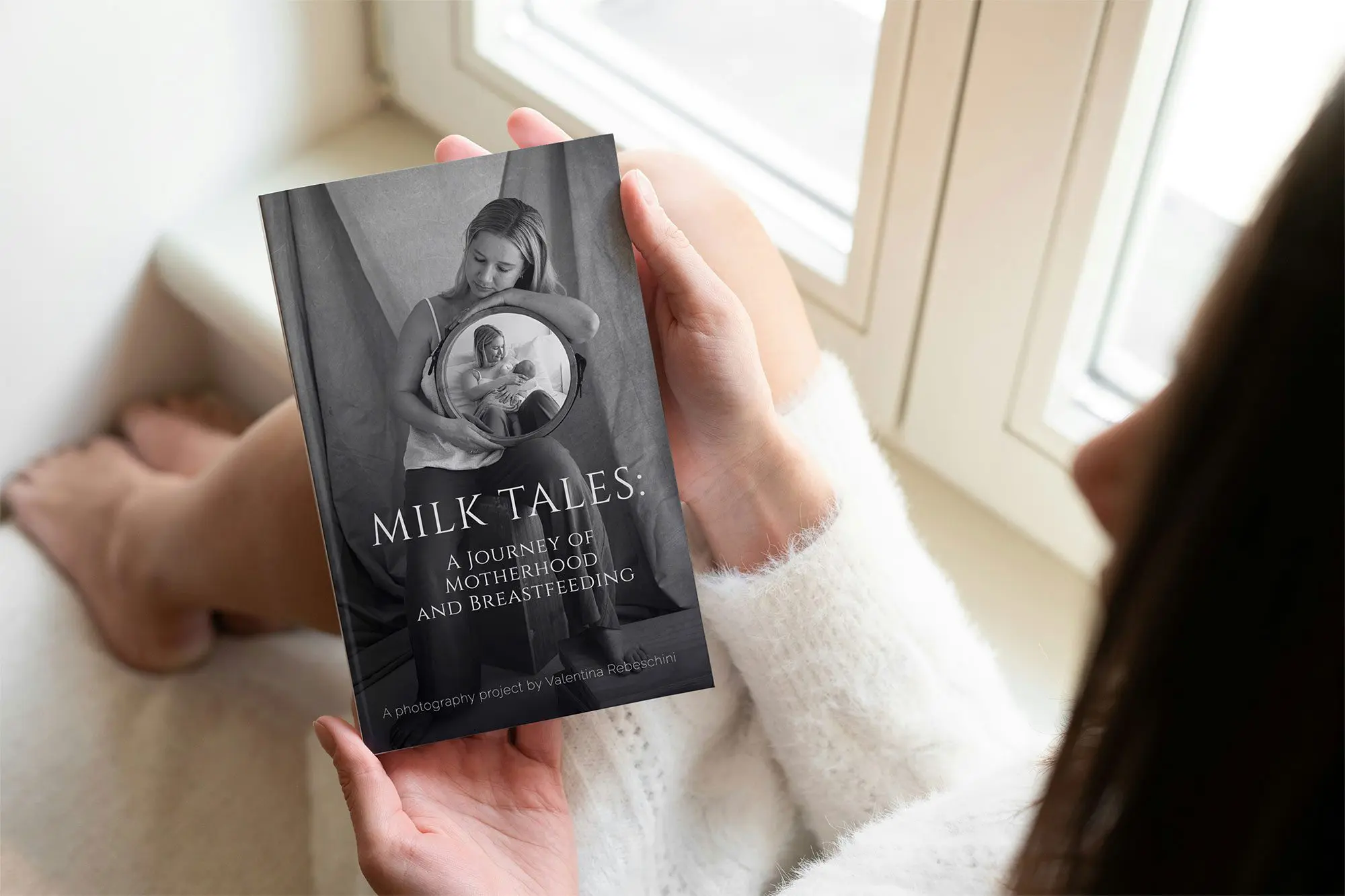 Close-up of a woman holding Milk Tales, a breastfeeding photography book by Valentina Rebeschini, featuring real stories and portraits of motherhood.