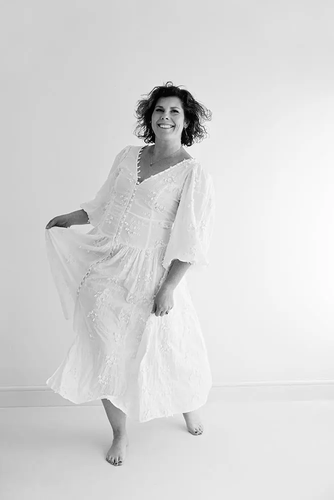 Joyful woman over 40 dancing in white dress during confidence building photography session, celebrating self-love and beauty