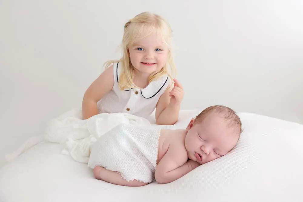 Older sibling holding newborn baby during family photography session showing sibling bond