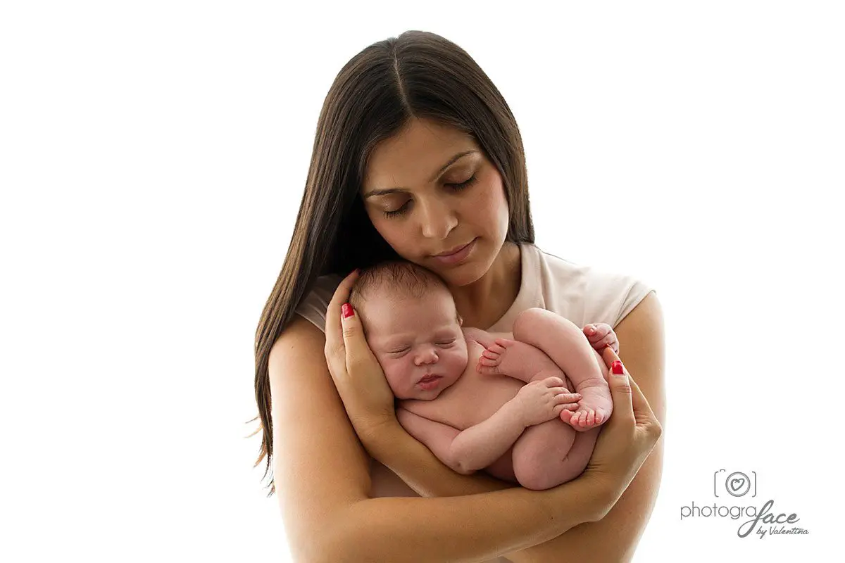 Mother gently holding her sleeping newborn close to her chest, eyes closed in a peaceful embrace