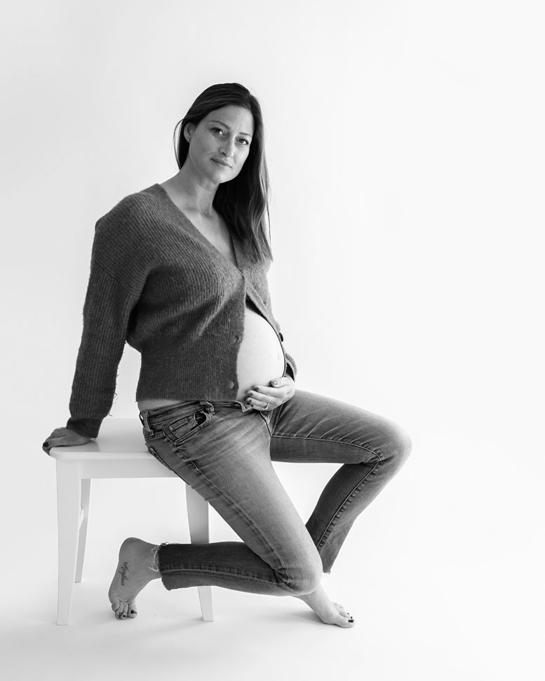 pregnant woman sitting on a stool and holding her baby belly