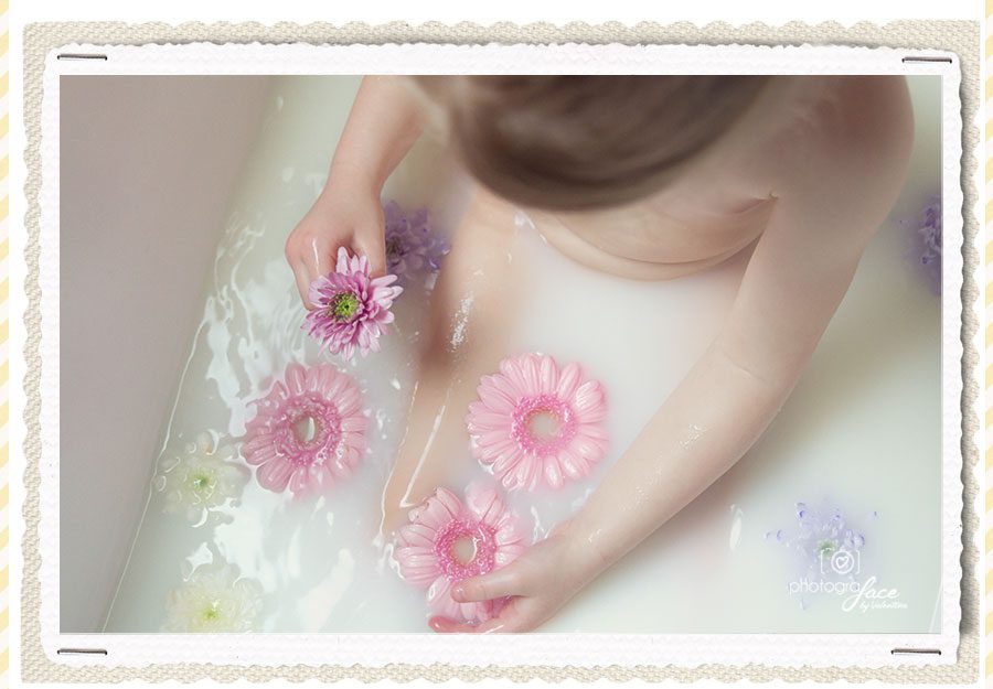 child in milky water playing with pink flowers