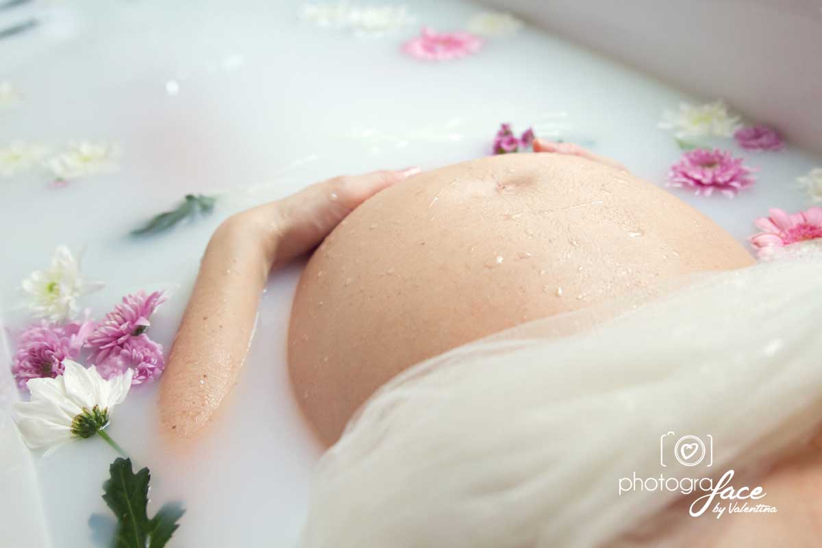 close up of pregnant belly in a milky bath with flowers