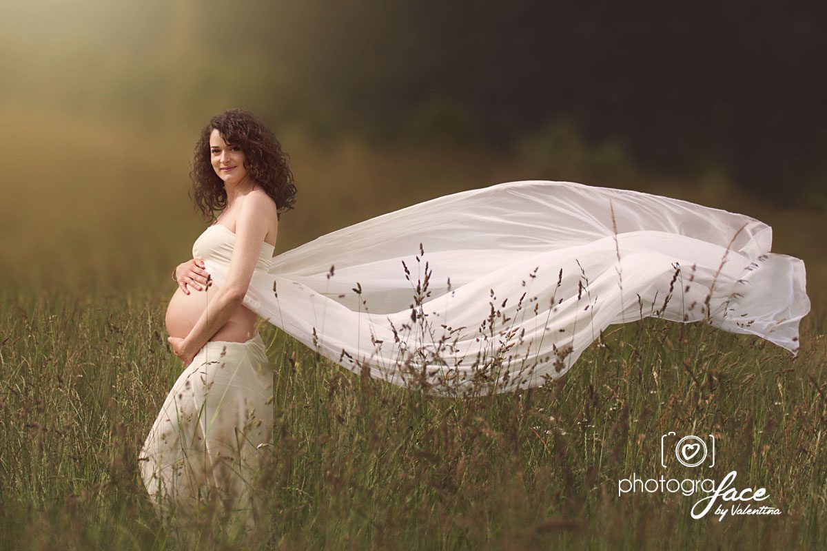 pregnant mum standing in a field with a flowy white dress