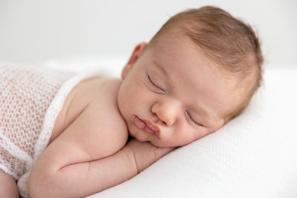 Newborn baby sleeping peacefully on a white blanket, captured by newborn photographer London – Photography by Valentina.