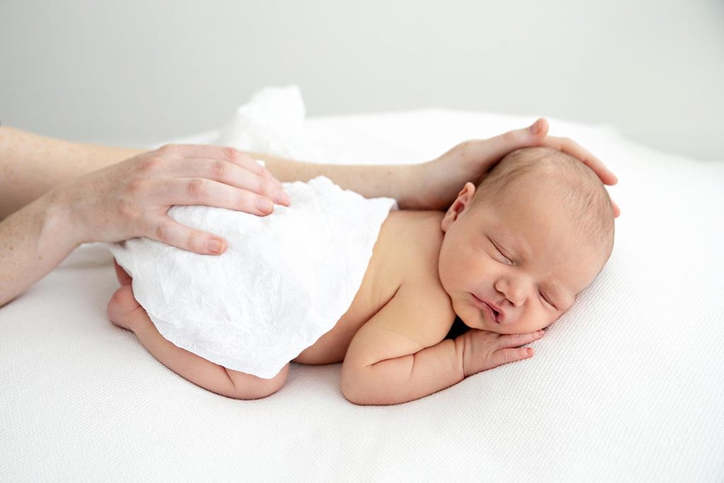 newborn sleeping on his tummy and mum's hands on his head