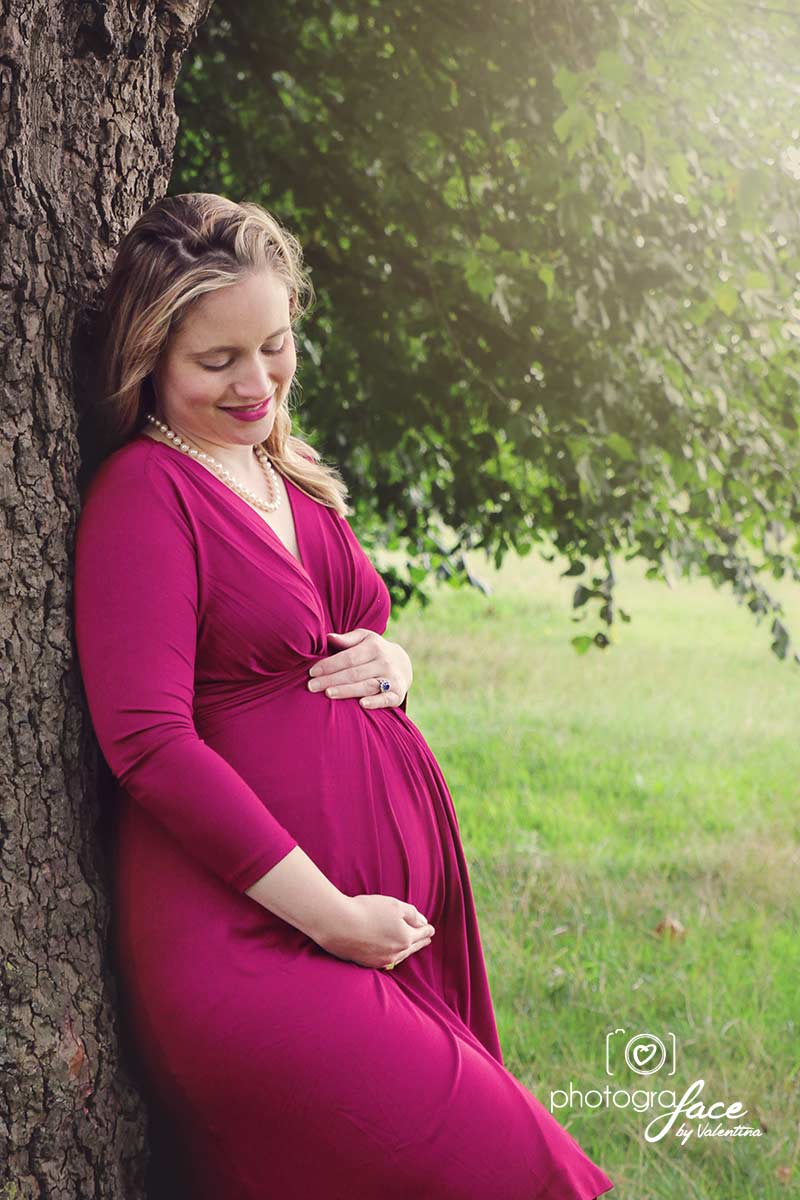 Pregnant woman under a tree in Clapham Common with her hands around the belly