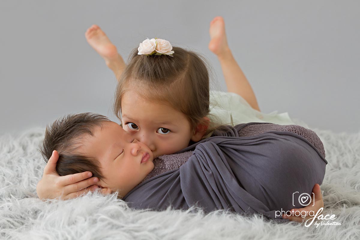 sister kissing newborn brother during a photoshoot