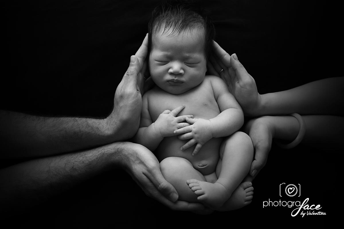 newborn curled on a black blanket with parents hands around him