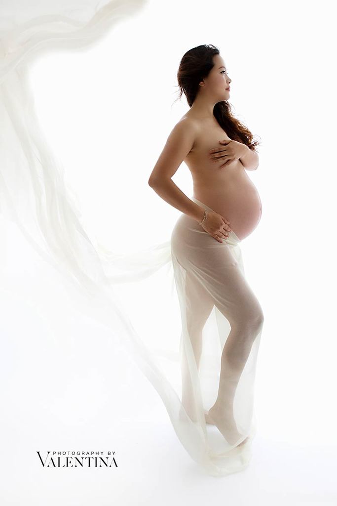 beautiful pregnant mum to be covered by white chiffon material leaving her baby belly exposed.