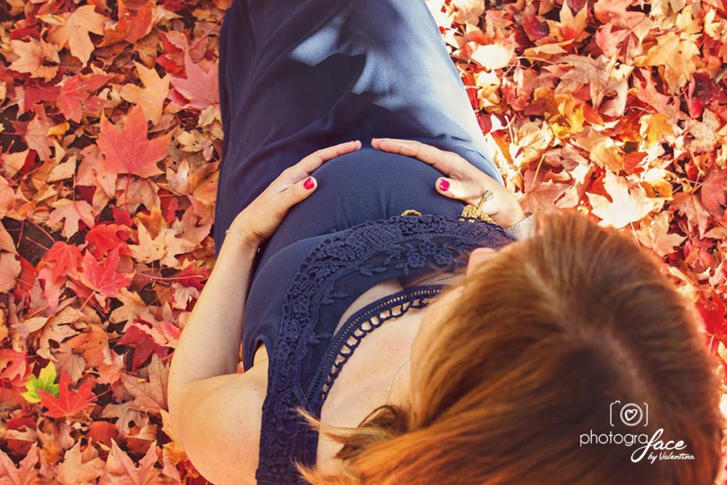 photo from above of a pregnant mum sitting within a bed of red leaves
