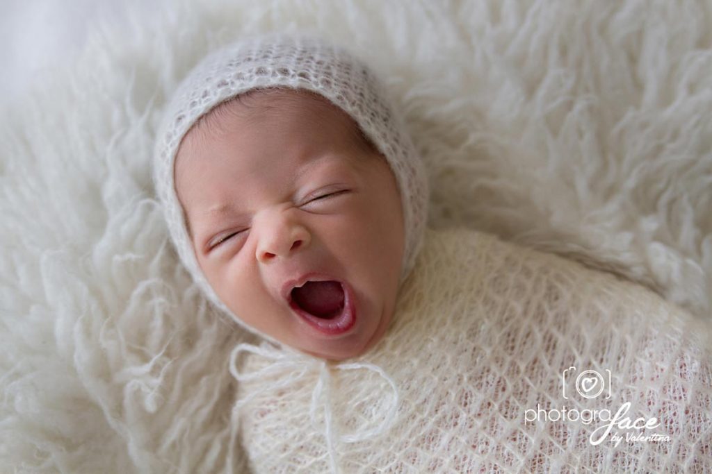 How soothe newborn baby. Little baby girl yawning. She is wearing a white soft moair hat and a matching swaddle.