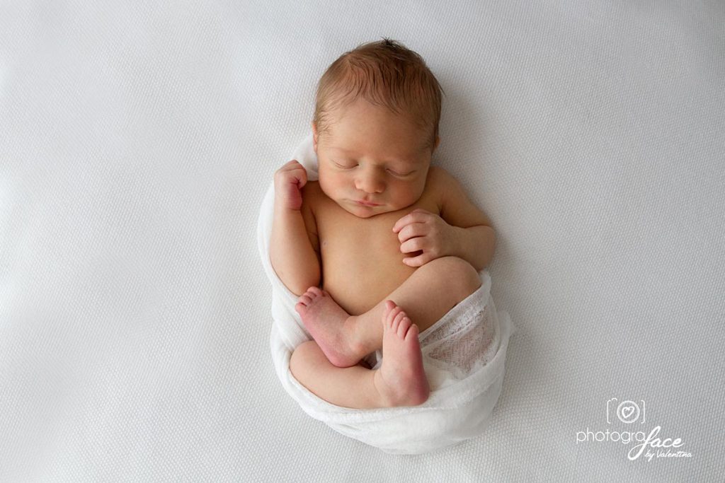 newborn photography - baby sleeping on his back wrapped on a white material on a white blanket