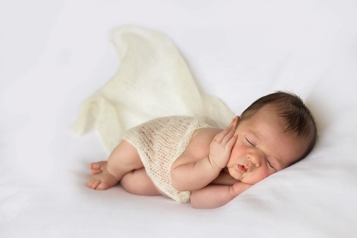 newborn sleeping with hands under his face on white blanket - london newborn photographer