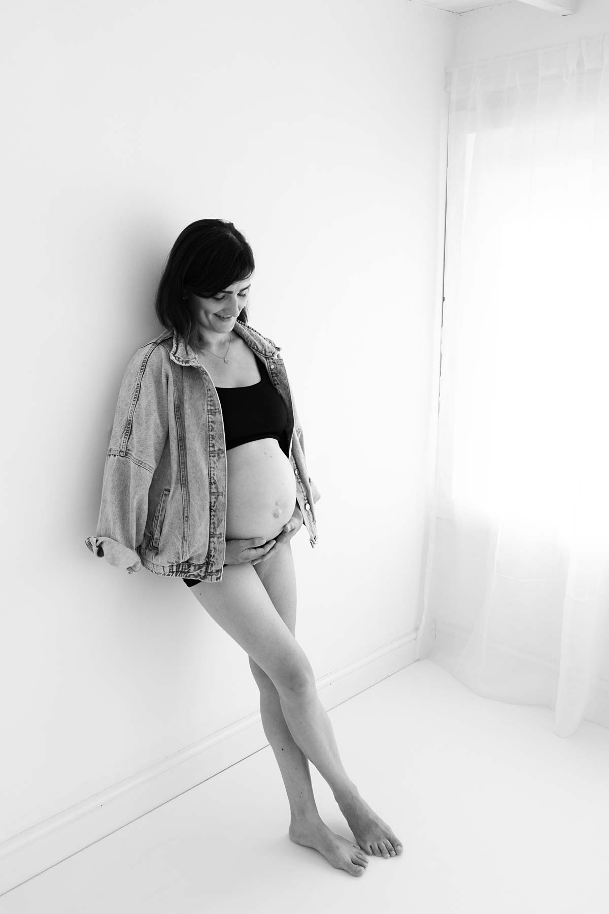 black and white maternity photo. Mum is laying on a wall and wearing a denim jacket and underwear