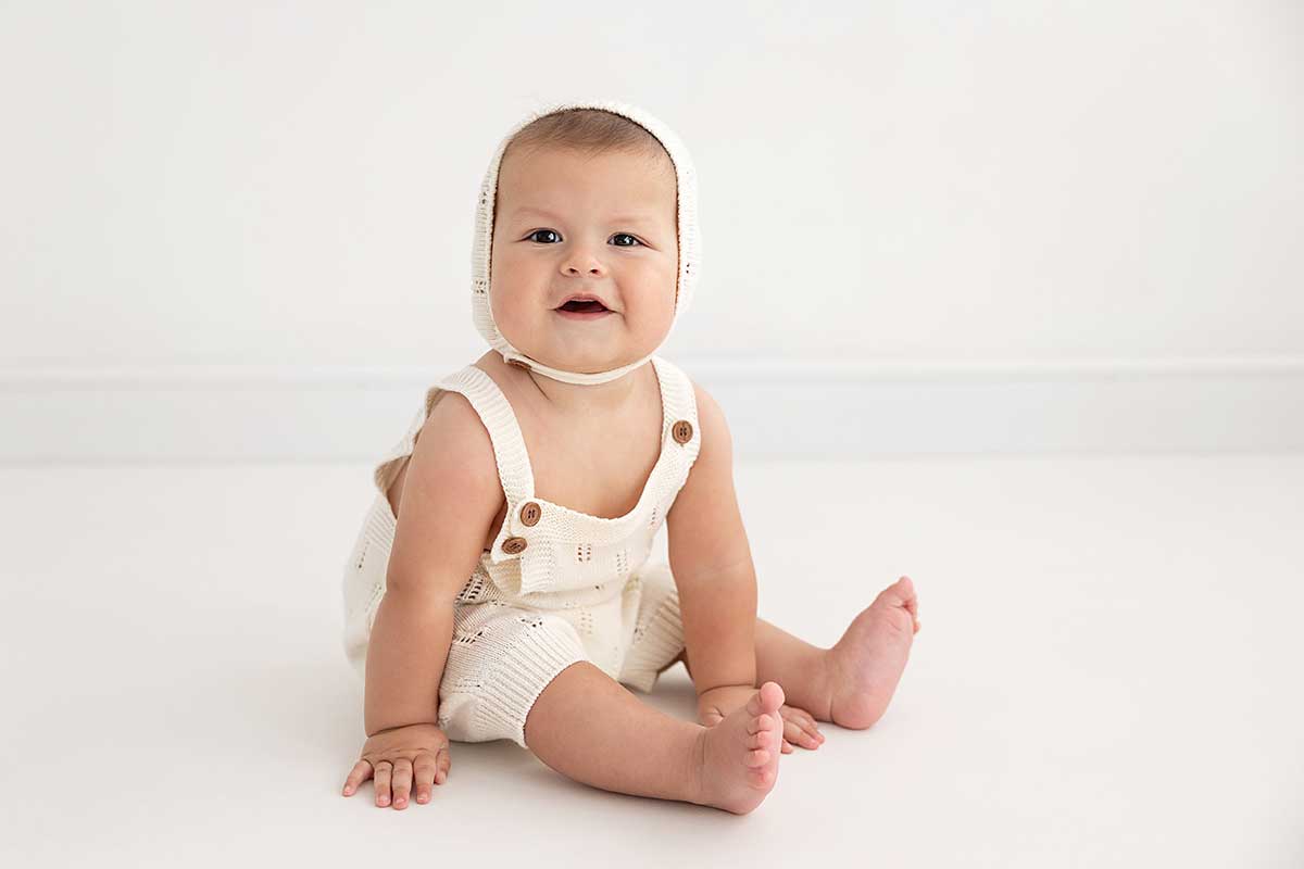 8 month-old baby sitting on a white floor in a cute romper during his photoshoot