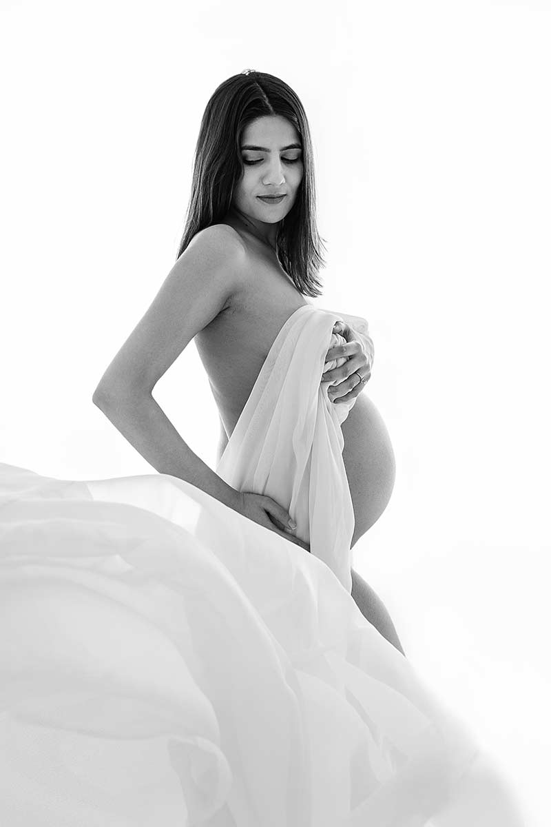 stunning photo of pregnant mum taken during her maternity photoshoot. She is wearing only a piece of fabric that is flowing in front of her living only the baby belly visible.