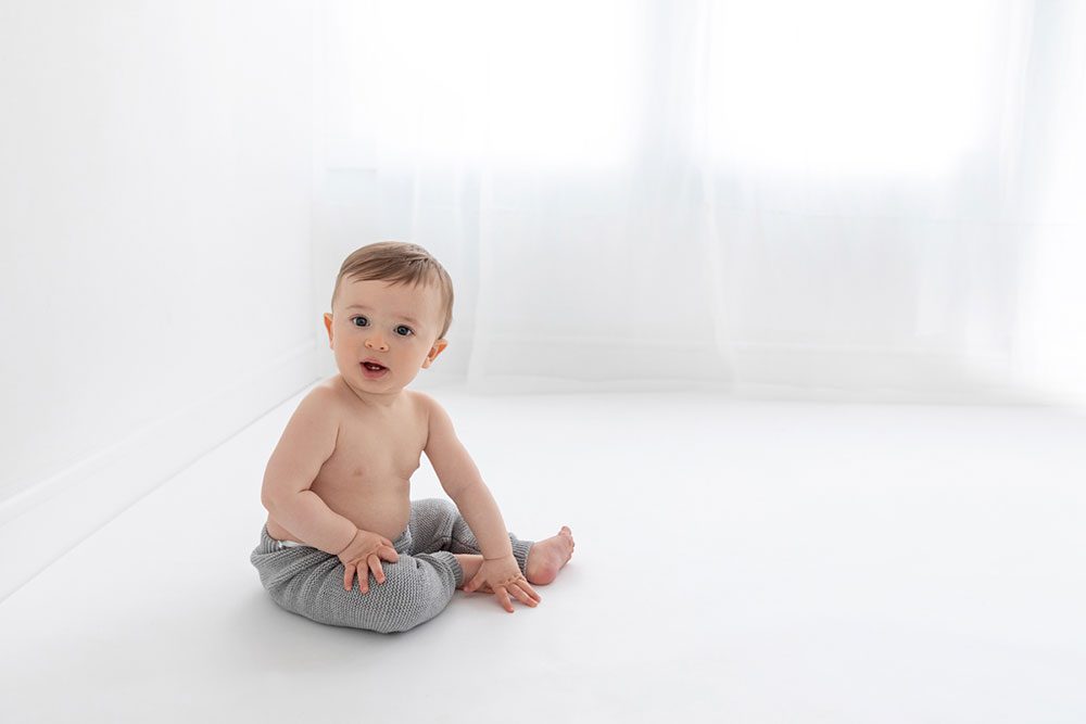 6 month old baby boy sitting on the white floor of a studio.