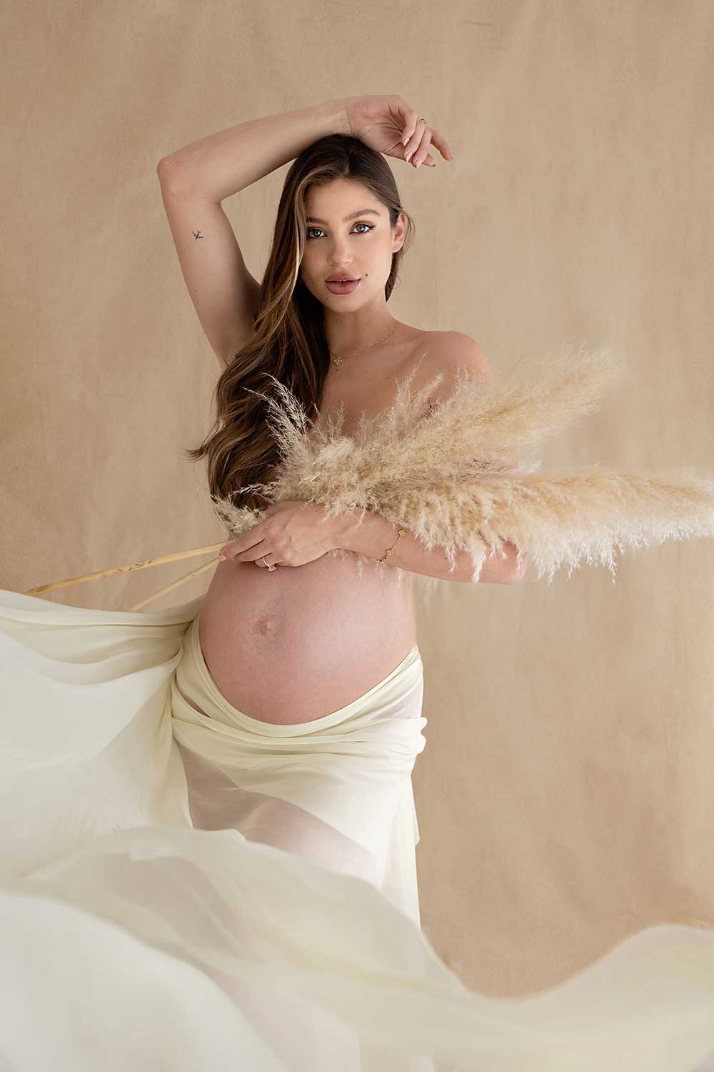 pregnant mum holding pampas to cover her breast and wearing a flowy fabric on her waist