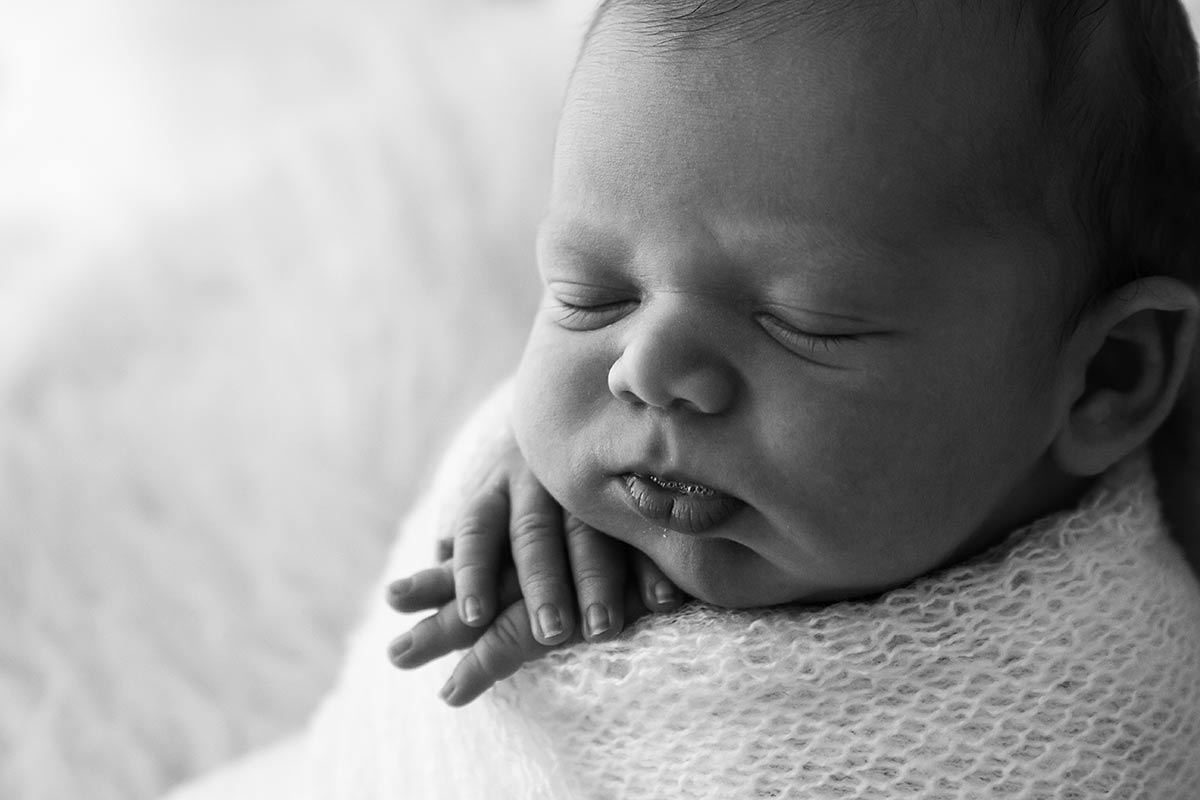 newborn baby wrapped in a soft white fabric with his hands out under his chin