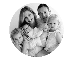 black and white family portrait: mum holding newborn baby and dad with the other 2 girls around her