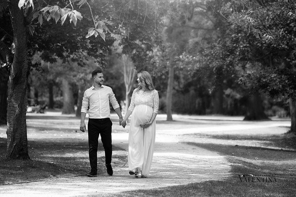 pregnant couple walking in the park. Mum is wearing a white maxi dress showing off her pregnant belly