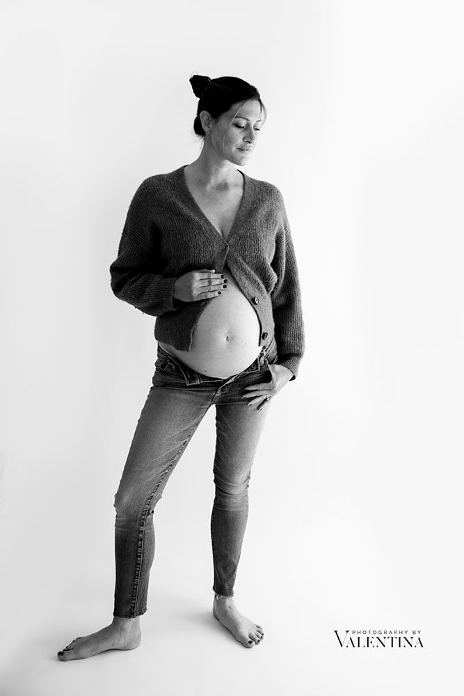 Pregnant mum wearing unbuttoned jeans and woollen cardigan open up on the belly.