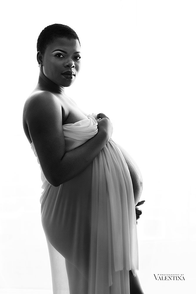 black and white image of a pregnant mum holding a white piece of fabric around her body. London maternity photographer 