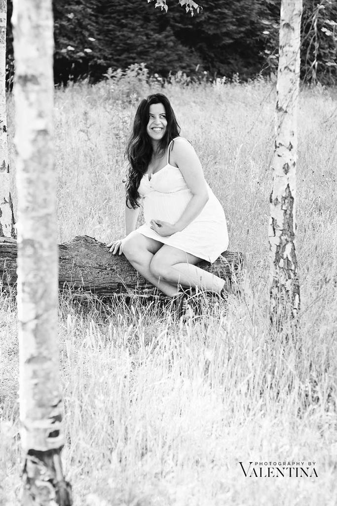 black and white image of pregnant mum sitted on a tree log looking up to the sky