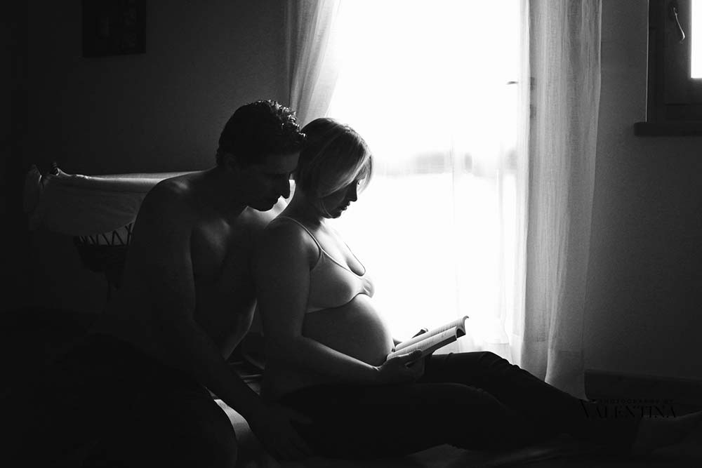 black and white of pregnant couple sitting on the floor and reading a book