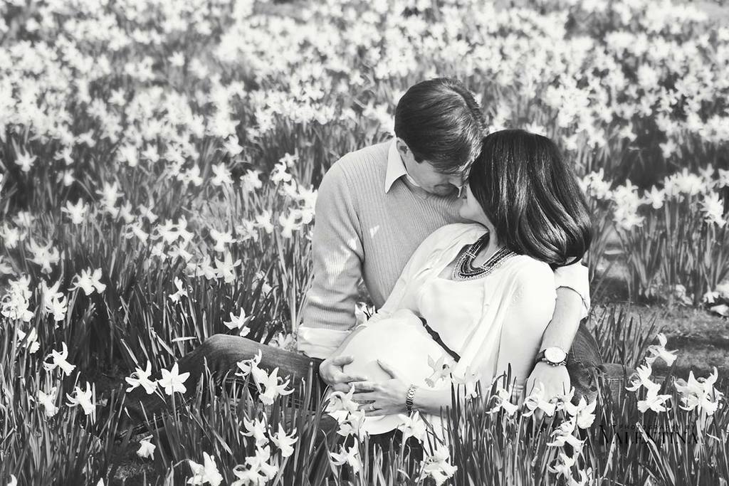 black and white image of expecting couple sitting on a field of daffodils