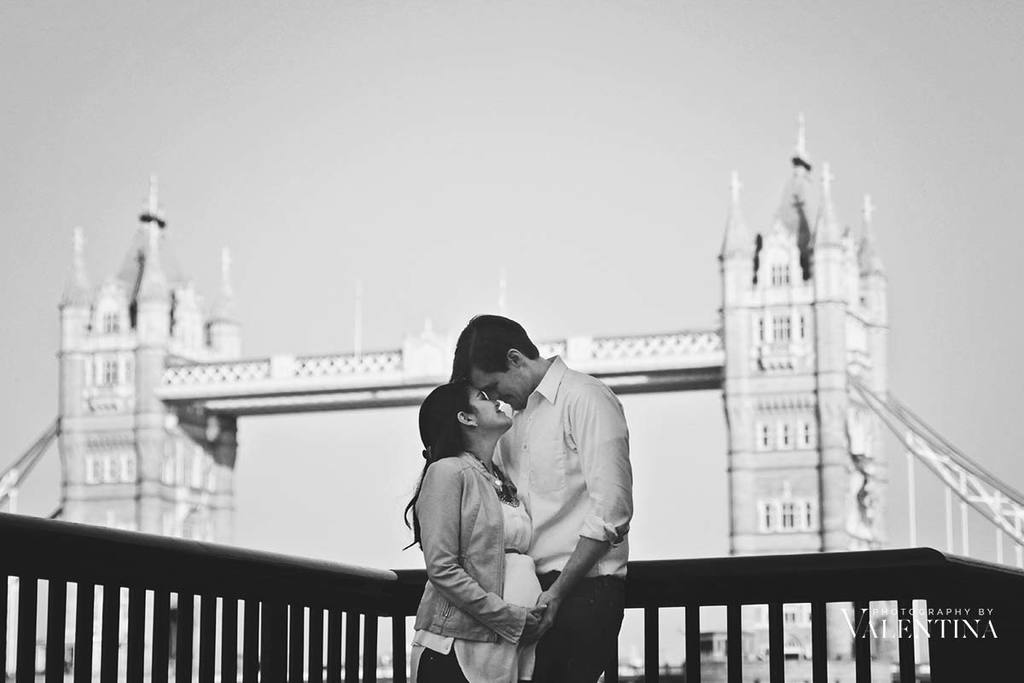 black and white portrait of pregnant couple looking at each other in front of the tower bridge