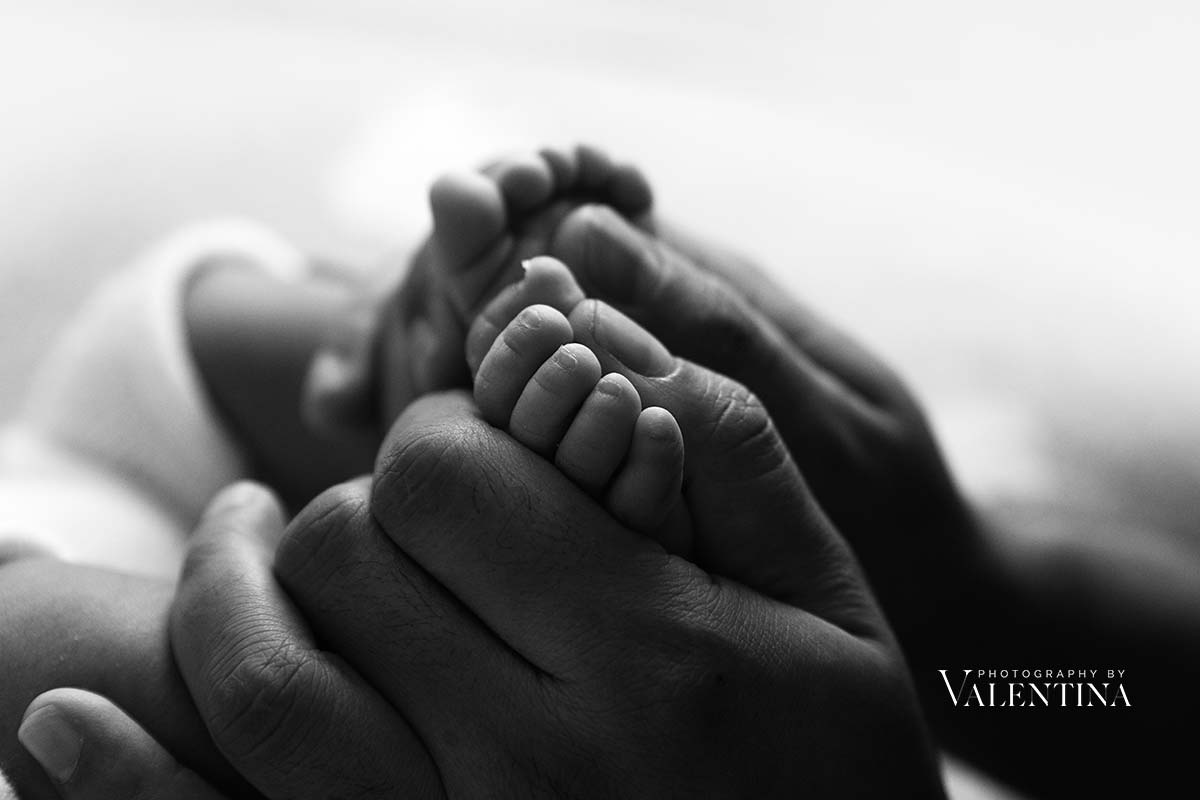black and white photo of newborn feet hold in mum's hands