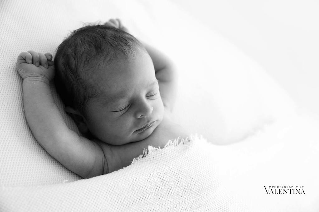 Black and white image of a newborn sleeping with his arms high. Photo take in the studio of Photography by Valentina, newborn photographer in Richmond
