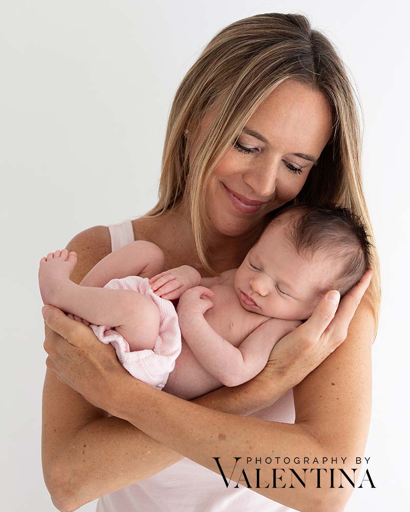Mum holding her newborn baby in her hands. The baby is sleeping and she is looking at her. Photo taken during a newborn photoshoot in Richmond