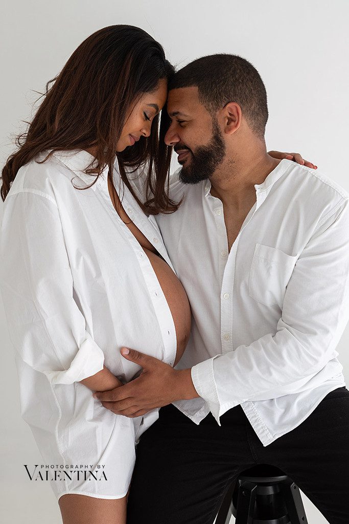 Sweet and tender image of pregnant couple. They are gently looking at each other while holding their hands on the pregnancy belly. This is why maternity photos are worth it.