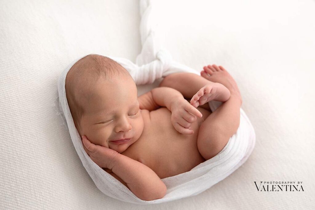 Newborn laying on his back on a white blanket and wrapped as if he was in the womb.