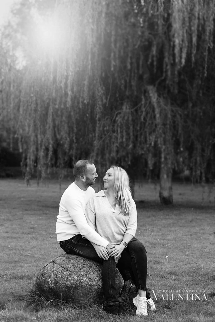 Black and white couple portrait. They are sitting on a stone on a park and looking at each other. Photo taken during a photoshoot with Valentina.