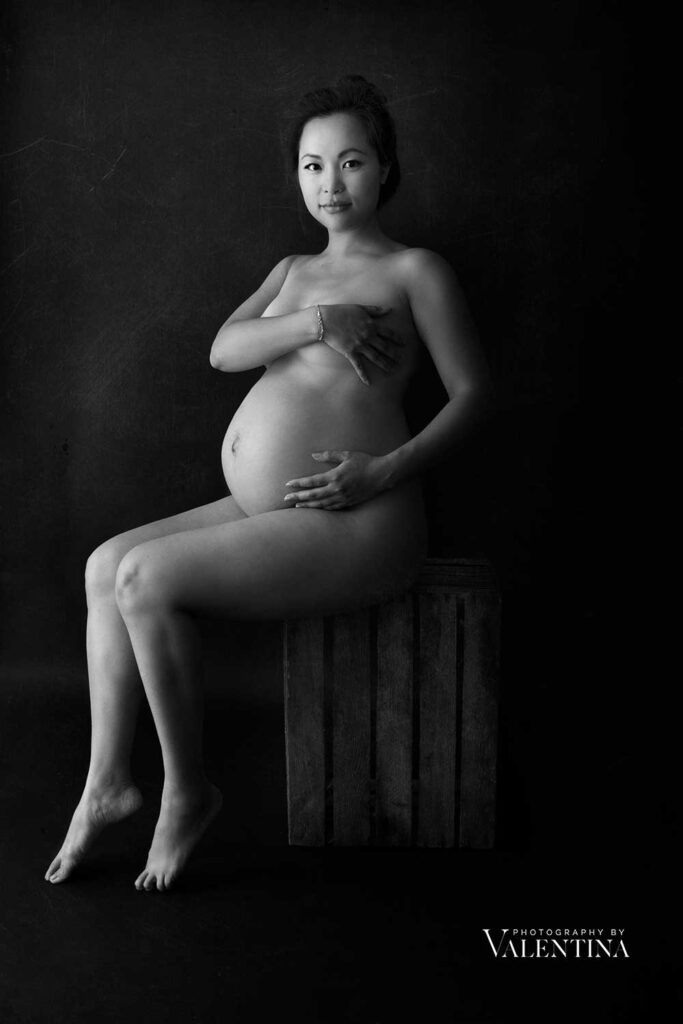 black and white portrait of pregnant woman naked sitting on a crate. The photo was taken during a maternity shoot in London