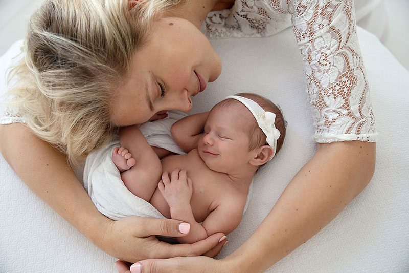 New mother lovingly embracing her smiling newborn baby girl wrapped in white, during a peaceful newborn photoshoot in London